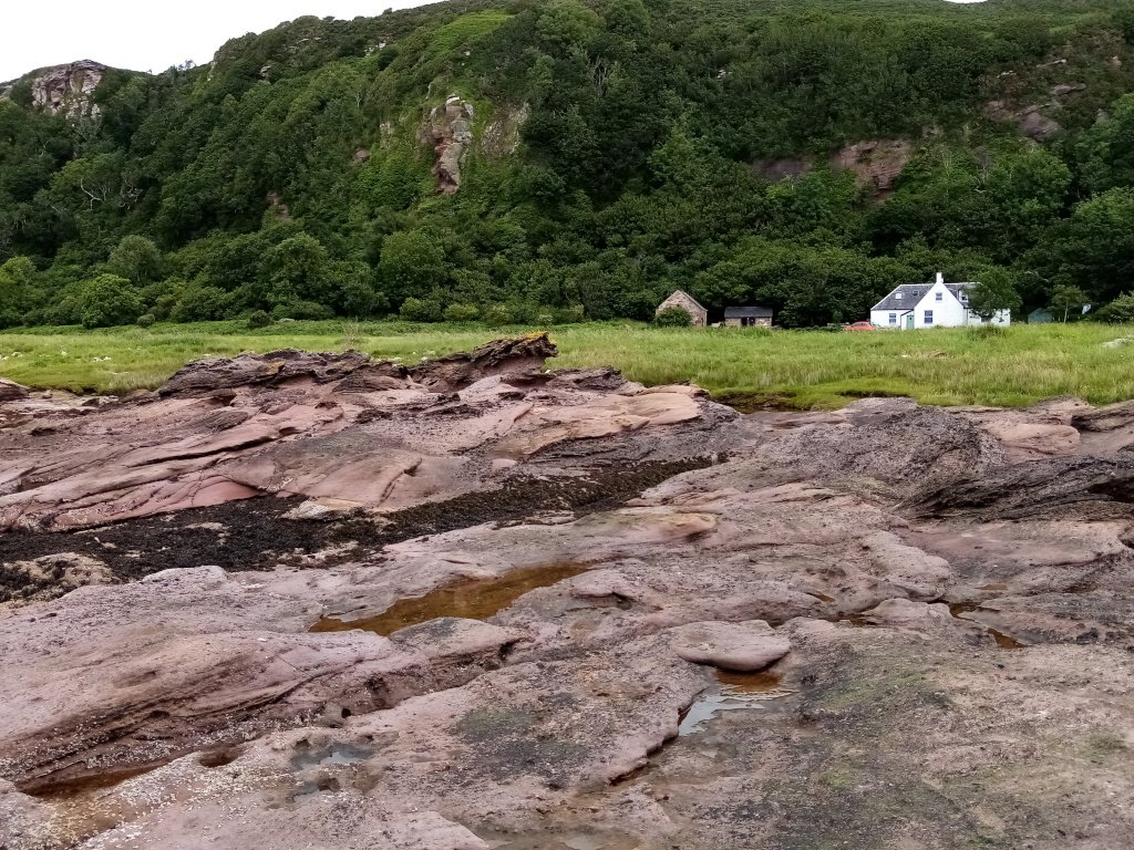 rocky foreshore with grassy area behind and cottage
     at base if cliffs